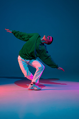 Image showing Stylish sportive boy dancing hip-hop in stylish clothes on colorful background at dance hall in neon light. Youth culture, movement, style and fashion, action.