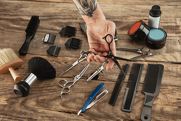 Image showing Hand of male barber with equipment set isolated on wooden table background.