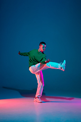 Image showing Stylish sportive boy dancing hip-hop in stylish clothes on colorful background at dance hall in neon light. Youth culture, movement, style and fashion, action.