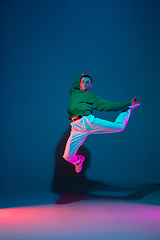 Image showing Stylish sportive boy dancing hip-hop in stylish clothes on colorful background at dance hall in neon light. Youth culture, movement, style and fashion, action.