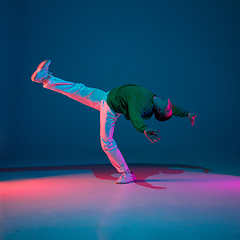 Image showing Stylish sportive boy dancing hip-hop in stylish clothes on colorful background at dance hall in neon light. Youth culture, movement, style and fashion, action.