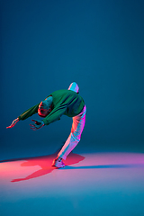 Image showing Stylish sportive boy dancing hip-hop in stylish clothes on colorful background at dance hall in neon light. Youth culture, movement, style and fashion, action.