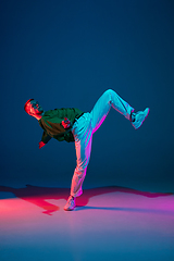 Image showing Stylish sportive boy dancing hip-hop in stylish clothes on colorful background at dance hall in neon light. Youth culture, movement, style and fashion, action.