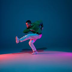 Image showing Stylish sportive boy dancing hip-hop in stylish clothes on colorful background at dance hall in neon light. Youth culture, movement, style and fashion, action.