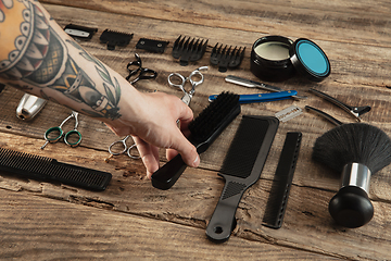 Image showing Hand of male barber with equipment set isolated on wooden table background.