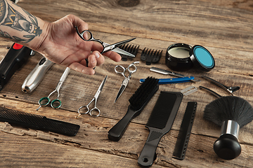 Image showing Hand of male barber with equipment set isolated on wooden table background.