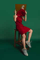 Image showing Female model in red outfit on green background with mirror. Style and beauty concept. Close up.