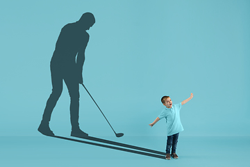 Image showing Childhood and dream about big and famous future. Conceptual image with boy and shadow of male golf player on blue background
