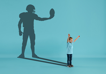 Image showing Childhood and dream about big and famous future. Conceptual image with boy and shadow of american football player on blue background