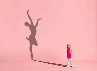 Image showing Childhood and dream about big and famous future. Conceptual image with girl and shadow of fit female ballet dancer on coral pink background