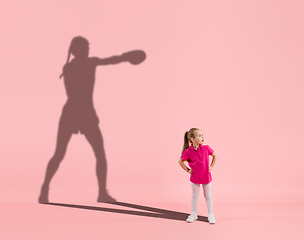 Image showing Childhood and dream about big and famous future. Conceptual image with girl and shadow of fit female boxer on coral pink background