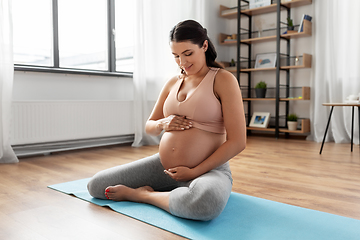 Image showing happy pregnant woman sitting on yoga mat at home