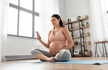 Image showing happy pregnant woman with phone doing yoga at home