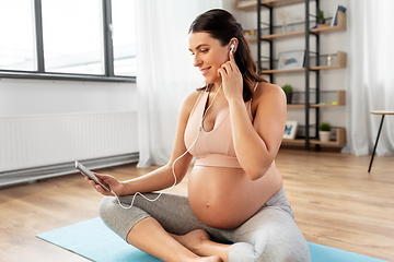 Image showing pregnant woman with earphones doing yoga at home