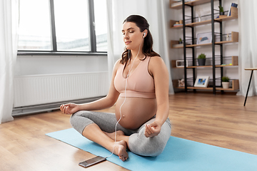 Image showing pregnant woman with earphones doing yoga at home