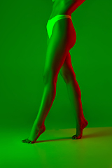 Image showing Beautiful female legs on green background in neon light. Beauty, cosmetics, spa, depilation, diet and treatment, fitness concept.