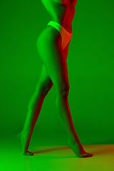 Image showing Beautiful female legs on green background in neon light. Beauty, cosmetics, spa, depilation, diet and treatment, fitness concept.