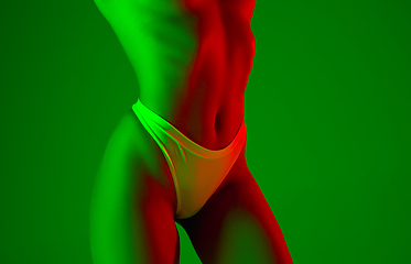 Image showing Beautiful female belly on green background in neon light. Beauty, cosmetics, spa, depilation, diet and treatment, fitness concept.