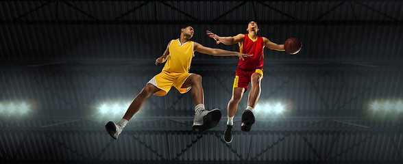 Image showing Young basketball players in competitive fight, motion in flight on black background, look from the bottom. Concept of sport, movement, energy and dynamic.