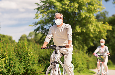 Image showing senior couple in masks riding bicycles at park