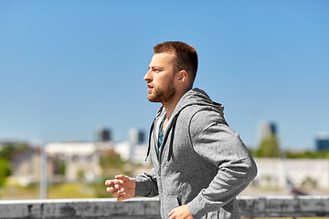 Image showing happy young man running across city bridge