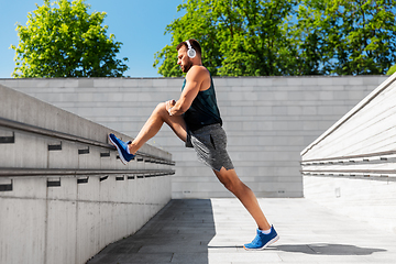 Image showing young man in headphones stretching leg outdoors