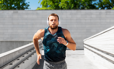 Image showing young man in headphones running outdoors