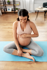 Image showing happy pregnant woman sitting on yoga mat at home