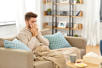 Image showing sick man blowing nose in paper tissue at home