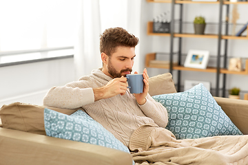 Image showing sick young man in blanket drinking hot tea at home