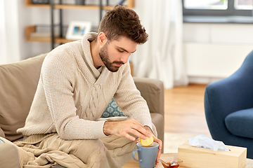 Image showing sick young man in blanket drinking hot tea at home