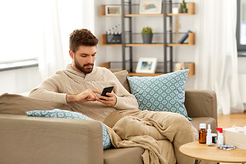 Image showing sick young man in blanket with smartphone at home