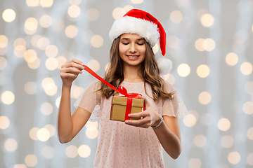 Image showing teenage girl in santa hat opening christmas gift