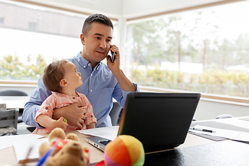 Image showing father with baby calling on phone at home office