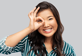 Image showing smiling asian woman looking through finger glasses