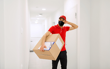 Image showing confused delivery man in mask with box in corridor