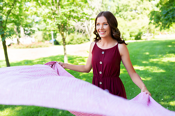 Image showing happy woman spreading picnic blanket at park