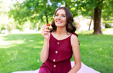 Image showing happy woman eating strawberry on picnic at park