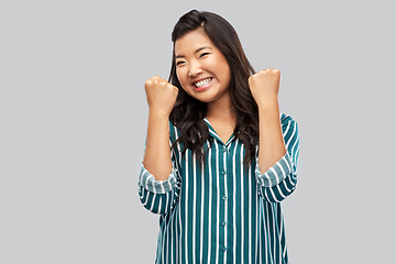 Image showing happy asian woman celebrating success over grey