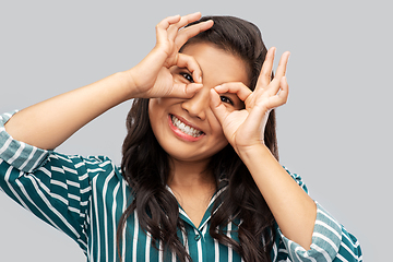 Image showing smiling asian woman looking through finger glasses