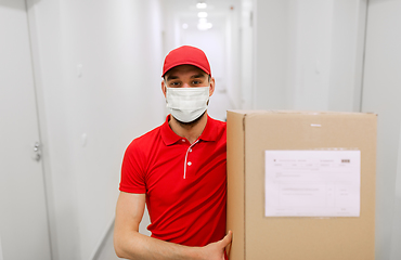 Image showing delivery man in mask with parcel box in corridor