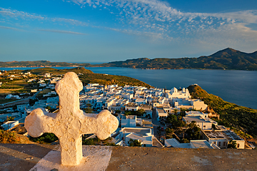 Image showing Christian cross and Plaka village on Milos island over red geranium flowers on sunset in Greece