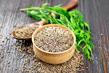 Image showing Cumin seeds in bowl and spoon with herbs on dark board