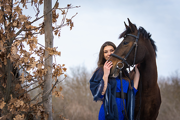 Image showing The girl peeks out from behind the muzzle of a horse, in the background an autumn forest