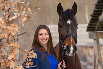 Image showing Close-up portrait of a horse and a beautiful girl of Slavic appearance, against the backdrop of a winter forest and an old farm