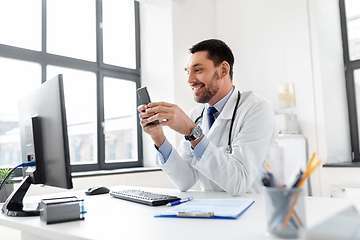 Image showing smiling male doctor with smartphone at hospital