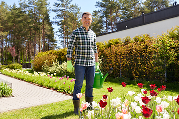 Image showing happy man with watering can and flowers at garden