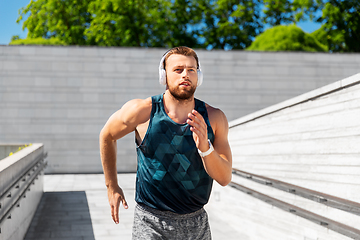 Image showing young man in headphones running outdoors