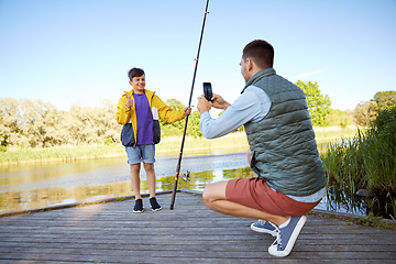 Image showing father photographing son with fishing rod on river