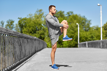 Image showing man stretching leg on bridge